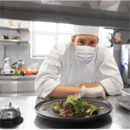 Chef wearing mask looking at camera through kitchen opening
