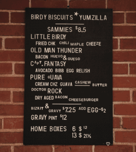 The Birdy Biscuits pop-ups menu board hung on a red brick wall