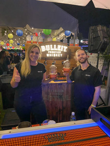 Bulleit Frontier Whiskey bartenders standing in front of their sign holding up bottles of whiskey