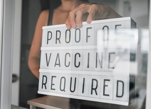 Vaccination proof vaccine passport required for entering store and restaurant as coronavirus restriction. Employee holding notice requirement sign in window of storefront.