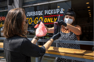 restaurant employee handing a to-go order over to a customer outside wearing masks