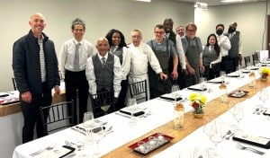 Proof of the Pudding team standing in a line in front of a white clothed table