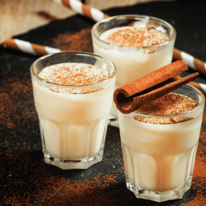 Alcoholic egg nog shots with cinnamon sticks on top.